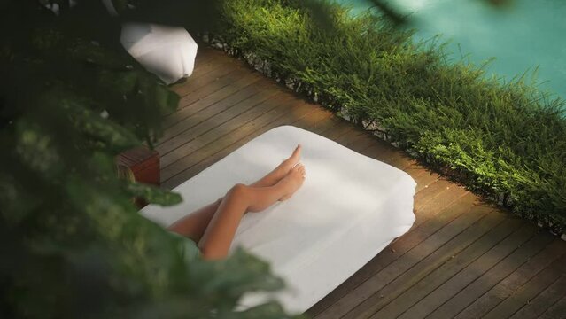 Slim caucasian female legs on white linen covered sun bed at pool, luxury concept