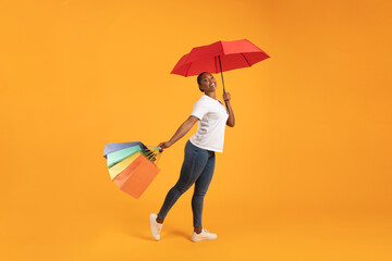 Black woman shopper stands with shopping bags and umbrella, studio