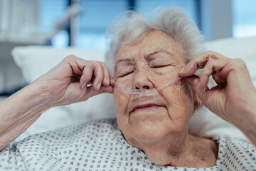 Senior woman after stroke, heart attack recoverying, lying in hospital bed. Elderly patient in hospital gown with nasal cannula.
