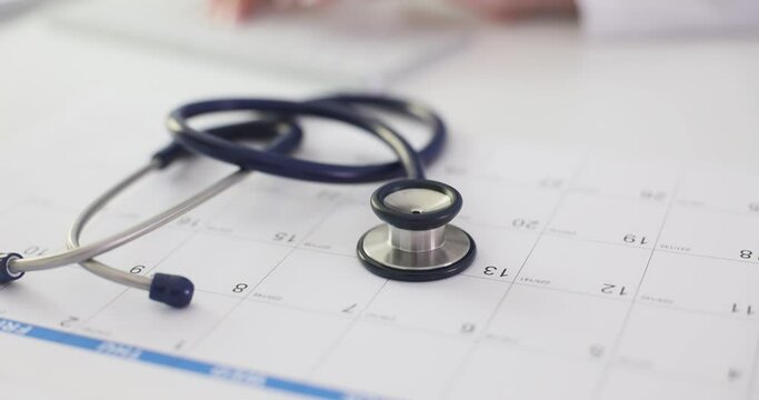 Stethoscope lying on doctor paper calendar in clinic closeup 4k movie slow motion. Annual medical checkup concept
