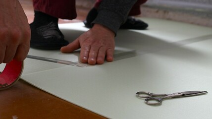 male hands glue together with transparent tape sheets of soft light-colored underlay for laminate...