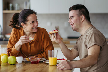 Young man with Down syndrome having breakfast with his mother at home. Morning routine for man with...