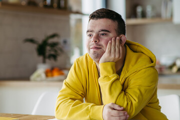 Young man with Down syndrome in kitchen, propping head up with his hand.