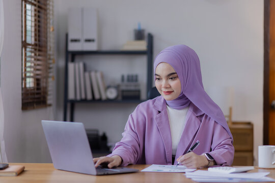 Asian islamic woman using laptop computer at desk in office.