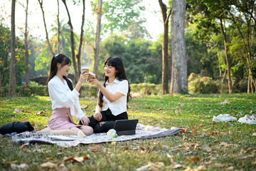 Two laughing young colleague clinking paper cups with coffee, resting in the park after work