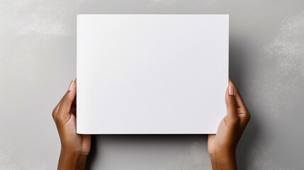 Top view of Woman's hand gracefully holding a blank white magazine on a gray background, serving as a design template mockup. - obrazy, fototapety, plakaty