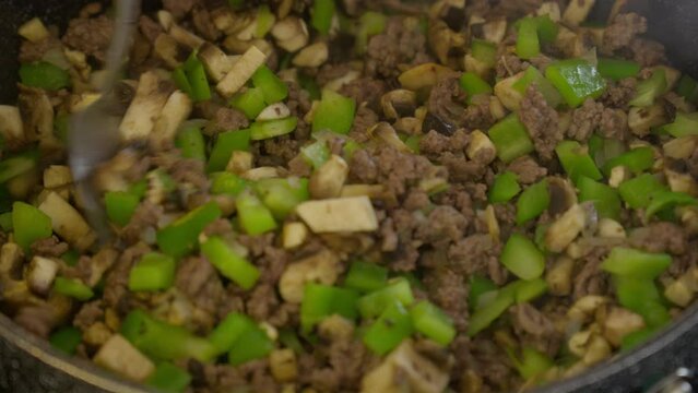 Men hand stri diced veggies mushroom and green bell pepper with hash brown beef in frying pan skillet with fork
