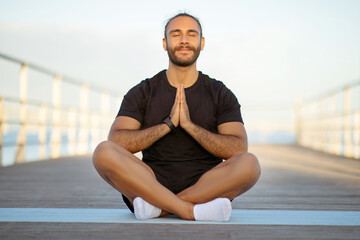 Peaceful fitness guy meditating with closed eyes at sea pier