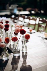 Red flower arrangements in vases, colorful decor, autumn flowers. On the festive table in the wedding banquet area, compositions of flowers and greenery, candles are placed.