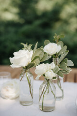 Many small white flower arrangements with roses, eustoma and various flowers in clear glass vases. On the festive table in the wedding banquet area, compositions of flowers and greenery, candles are p