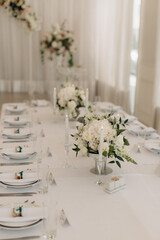 Many small white flower arrangements with roses, eustoma and various flowers in clear glass vases. On the festive table in the wedding banquet area, compositions of flowers and greenery, candles are p