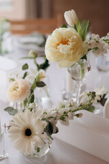 Many small white flower arrangements with roses, eustoma and various flowers in clear glass vases. On the festive table in the wedding banquet area, compositions of flowers and greenery, candles are p
