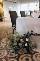 A large flower arrangement of white flowers for the newlyweds' table, decoration of the presidium. On the festive table in the wedding banquet area, compositions of flowers and greenery, candles are p