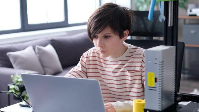 Young Caucasian scientist boy, doing homework, planning project or studying with laptop sitting at desk in home workshop. Invention designing and engineering concept.