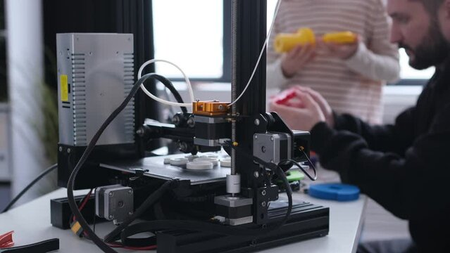 Close up shot of a modern 3D printer working at desk in workshop. Automated machine, printing mechanism or project plastic detail.