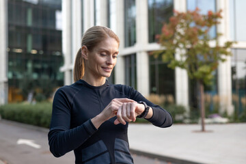 A focused female athlete pauses during her urban workout to monitor her performance on a...