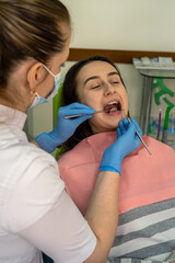Feamle dentist use dental instrument examining young woman patient's teeth at dental clinic