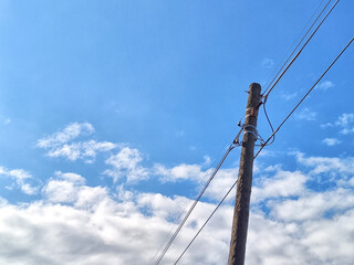 Old power line pole against blue sky in sunny day