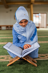 A Muslim child girl reading a Quran inside the mosque.