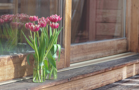 bouquet of tulips in vase in front of a bay window on wooden terrace