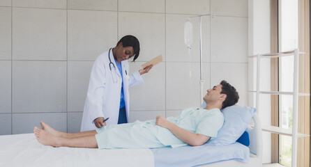 Portrait patient caucasian man lying bed with woman doctor African-American standing carer physical therapist two people talk helping support and check treat sick person inside hospital room service.