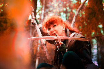 Mature model portraying a royal huntress with red curve hair is hunting with a crossbow in the in...