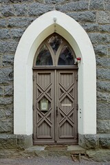 Fototapeta na wymiar Wooden double doors with a arch window with white frame on a stone building.