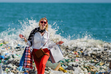 Modern woman on landfill with shopping bags. standing on pile of waste on beach. Consumerism versus...