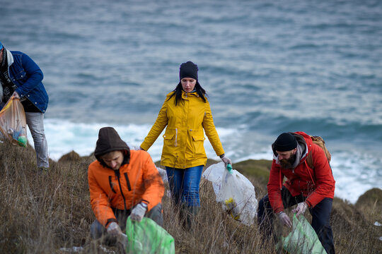 Group of activists picking up litter along riverbank. River clean up. Environmental pollution, eco activism. and plogging concept.