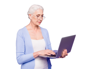 Gray haired old serious business woman wearing glasses, holding computer, typing texts, browsing. Isolated over violet purple background