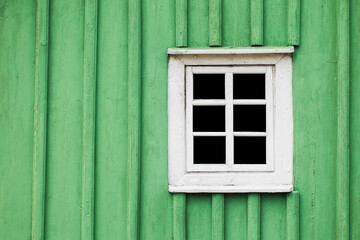 Rustic window in wooden village cottage house. Green wood wall. Countryside architecture background. Small window frame white paint. Empty copy space paint wall. Square shape window.