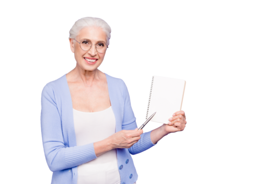 Gray haired old smiling business woman wearing glasses, showing blank page holding paper note book with pen. Isolated over violet purple background