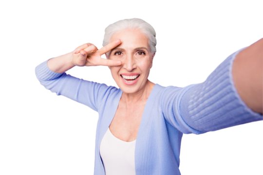 Elderly lady makes selfie on the camera of a smartphone making v-sign near the eyes isolated on bright violet background with copy space for text - Powered by Adobe