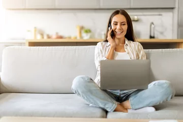 Tuinposter Remote Business. Young Woman Talking On Phone And Using Laptop At Home © Prostock-studio