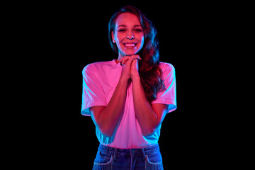 Happy and excited young woman in smiling, clapping hands against black studio background in neon...