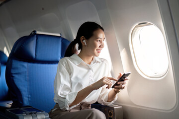 Fototapeta premium Traveling and technology. Flying at first class. Young business woman passenger using smartphone while sitting in airplane flight