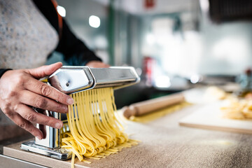 Close up of female hands preparing fresh pasta using traditional machine - Cuisine and food concept