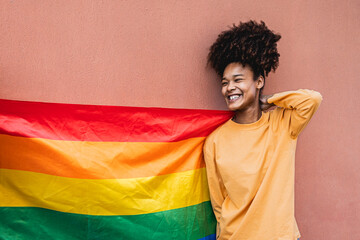 Happy African gay woman celebrating pride holding rainbow flag outdoor - LGBT concept