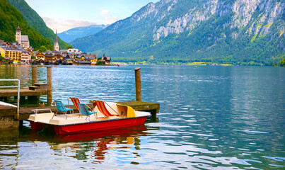 Hallstatt, Austria. Lake Hallstattersee with calm blue water among austrian Alps mountains. Embankment of antique picturesque town. View to old houses and chapel church. Pleasure boat in front.