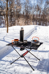 Tableware standing on the table in the winter forest, tourist cutlery set, camping tableware, folding table for hiking.