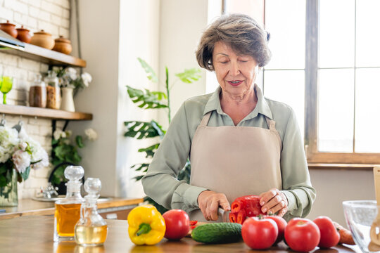 Caucasian mature elderly senior grandmother cooking salad at home kitchen. Old woman housewife cutting vegetables, preparing lunch dinner vegetarian soup - Powered by Adobe