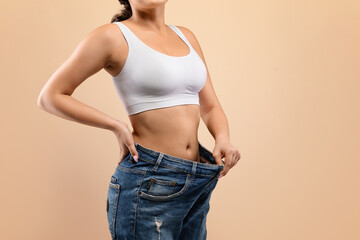 Fit woman confidently demonstrating successful weight loss by pulling out oversized jeans,