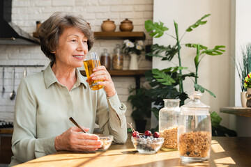 Caucasian senior grandmother drinking apple juice, maintaining healthy diet eating in the morning...