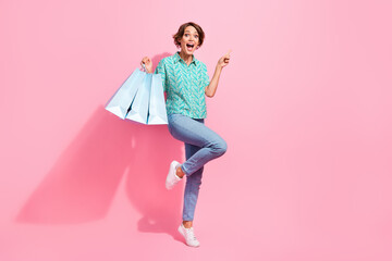 Full length portrait of astonished cheerful person hold store bags indicate finger empty space ad...
