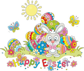 Greeting card with a happy Easter bunny and a pile of colorfully painted gift eggs on a pretty sunny lawn with spring flowers and merry butterflies fluttering around, vector cartoon illustration