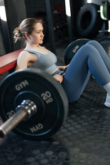 young girl in a tracksuit doing a glute bridge with a barbell in the gym