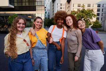 Multiracial group of smiling young women standing together embraced outdoors in an urban area....