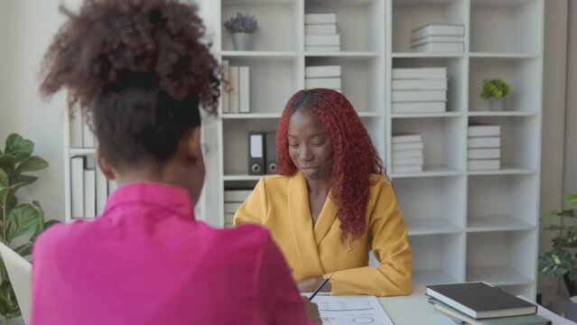 Two African American business women are talking in a private office, they are discussing about project that their boss ordered them to finish before the presentation day.
