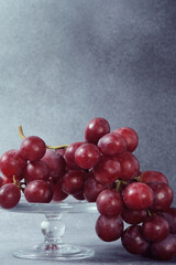 Fresh Red Grape Bunch on a Clear Glass Pedestal Against a Grey Textured Background