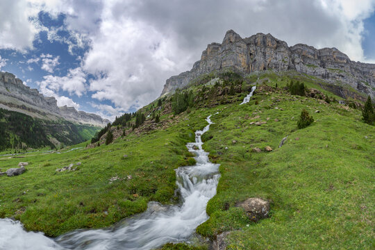Lush greenery and a vibrant mountain stream cascade down the rocky landscape of Valle de Ordesa, located in the Ordesa y Monte Perdido National Park